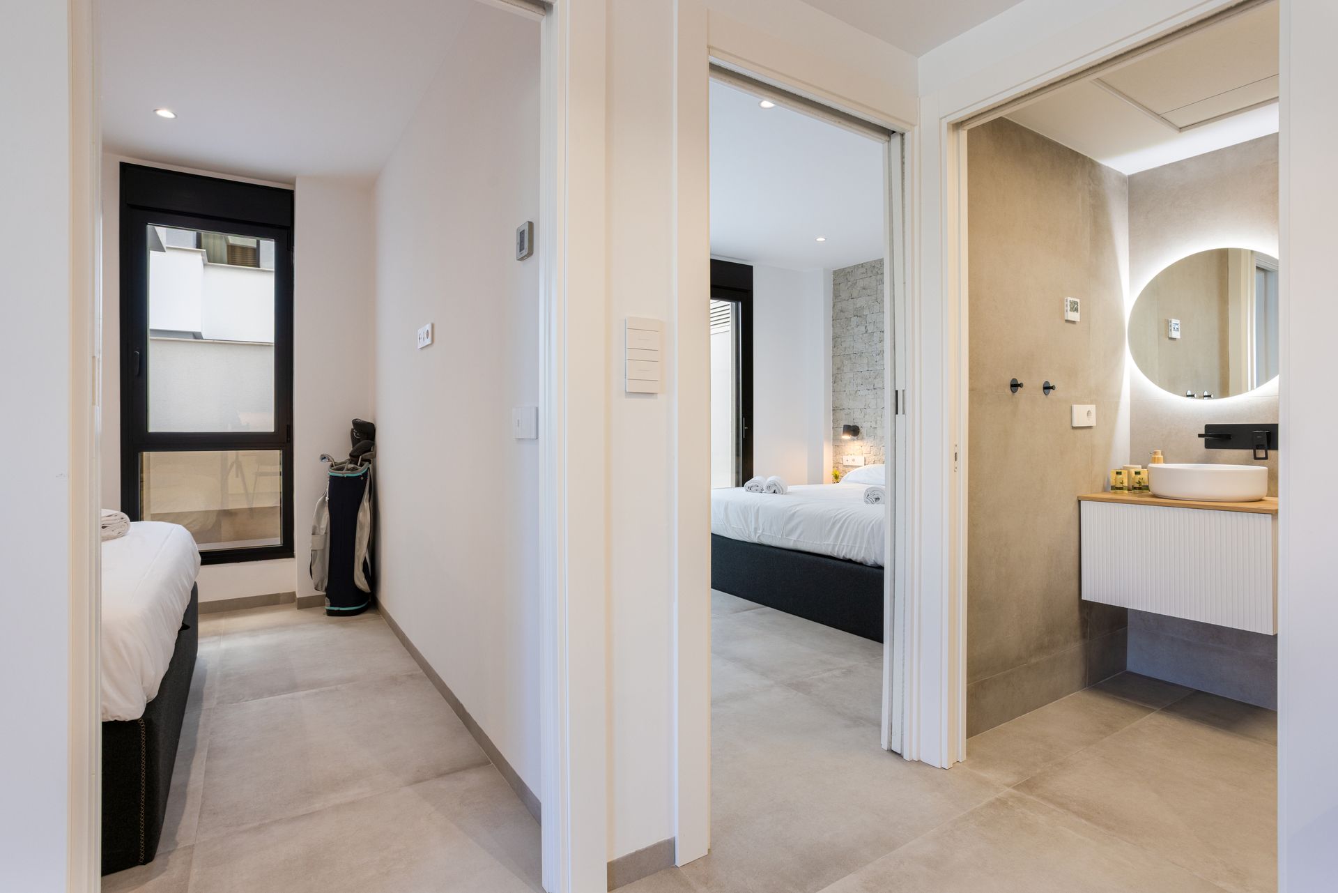 Bright hallway between two rooms, with a bedroom on the left and a bathroom vanity on the right.