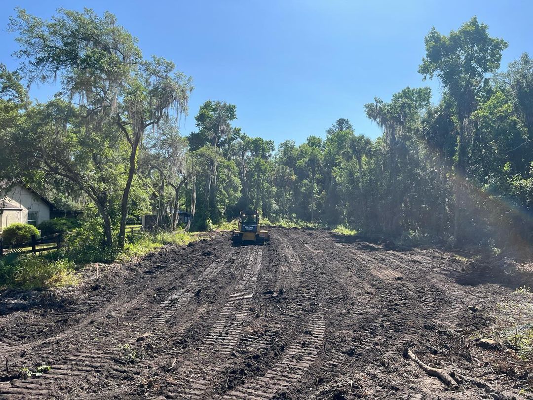 A bulldozer is driving down a dirt road surrounded by trees.