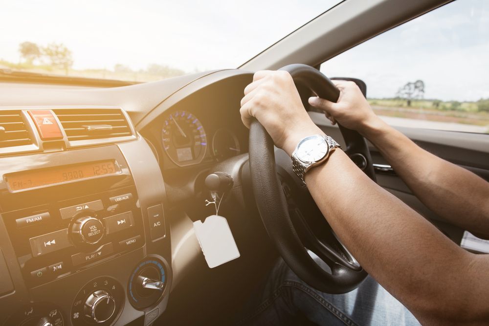 A Man Is Driving A Car With His Hands On The Steering Wheel — Airlie Beach Exhaust and Mechanical In Airlie Beach, QLD