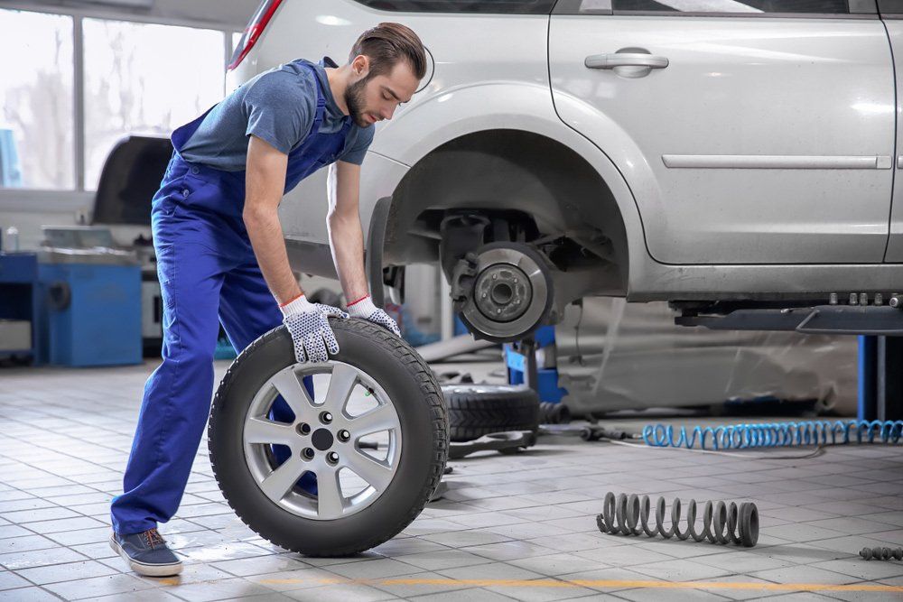 A Man Is Changing A Tire On A Car In A Garage — Airlie Beach Exhaust and Mechanical In Bowen, QLD