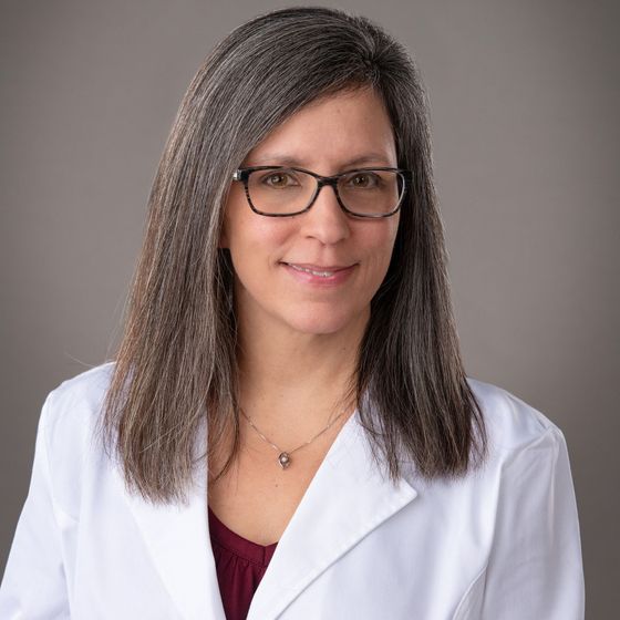 A woman wearing glasses and a white coat is smiling for the camera.