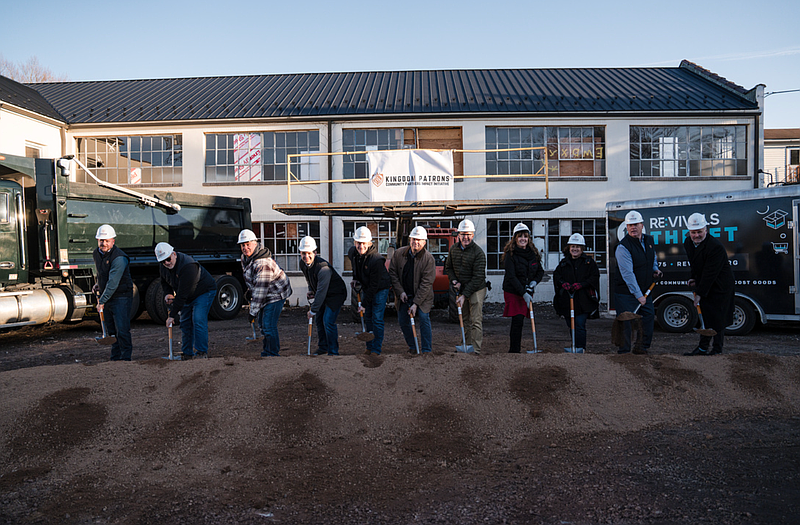 Group of people with shovels breaking ground in front of a building, possibly a construction site.