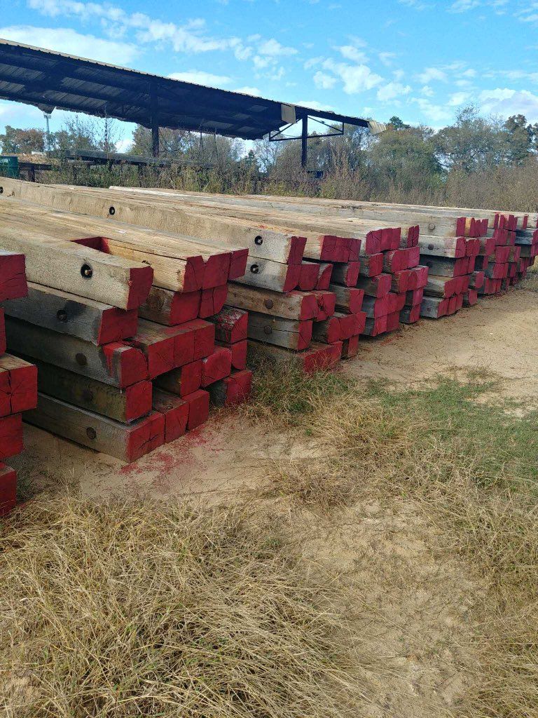 Stacks of red-topped wooden beams arranged outdoors beside a grassy field and a metal shelter.