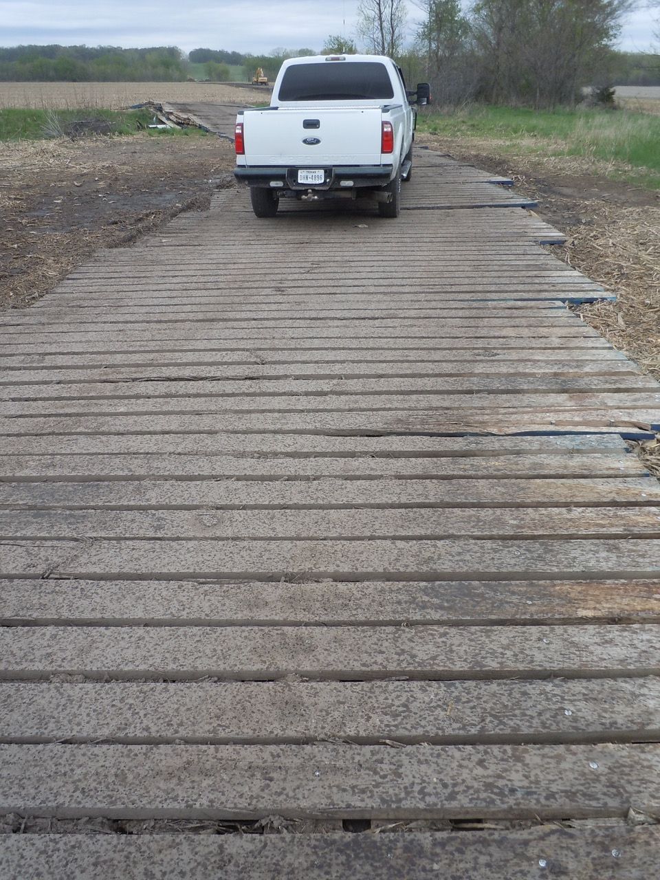 White pickup truck driving on a 3-ply laminated mat over a rural area