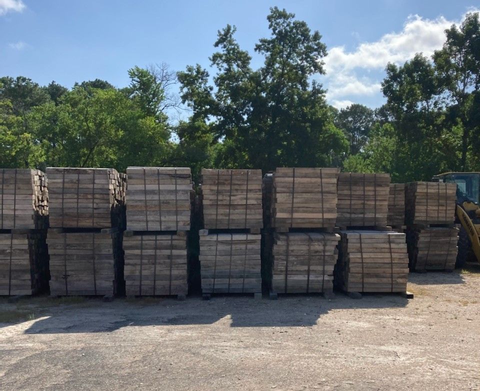 Stacks of used pipeline skids for sale in houston in an outdoor lot under a blue sky, with trees in the background