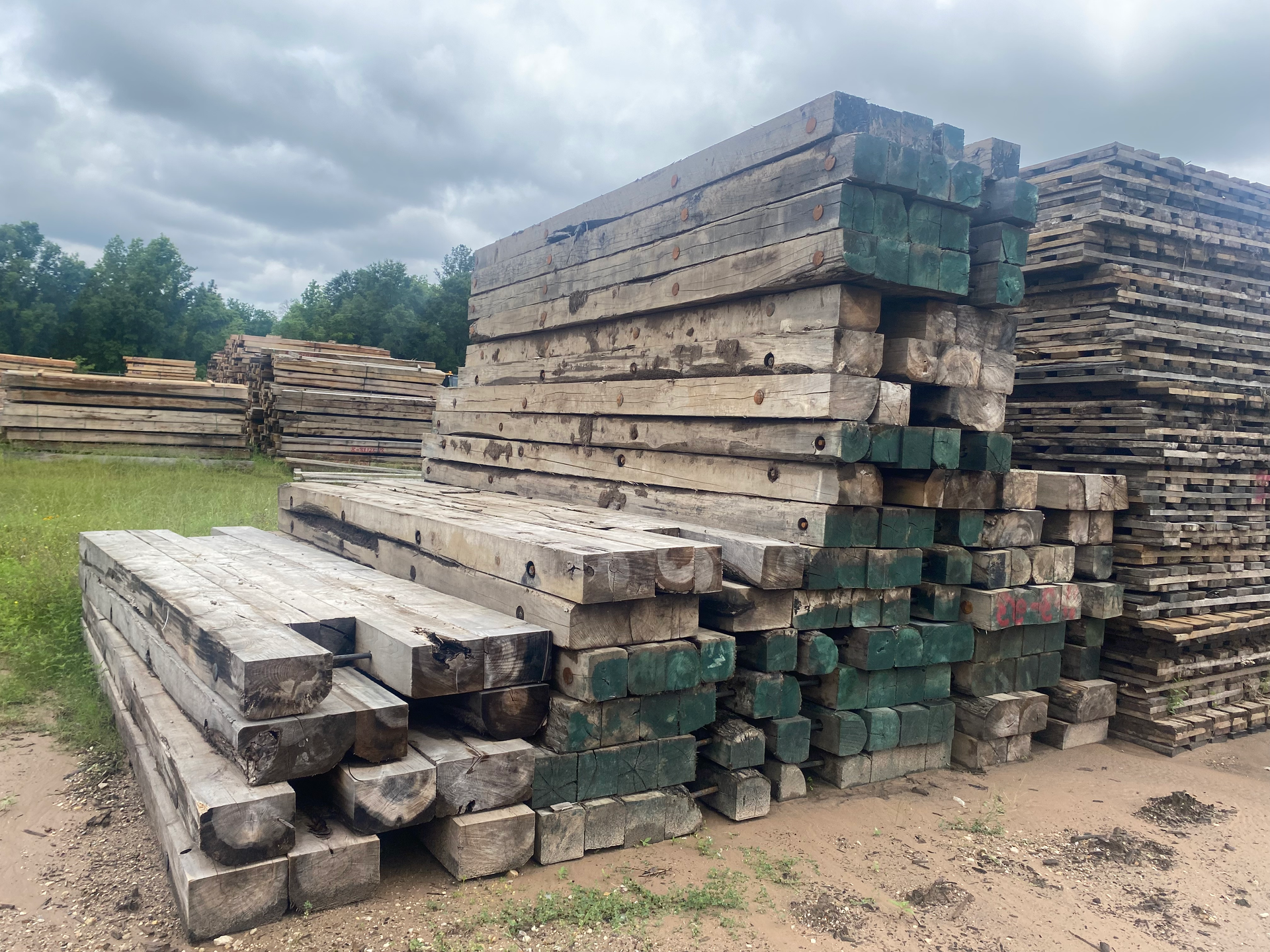 Stacks of used hardwood digging mats piled outdoors on a dirt lot under cloudy skies