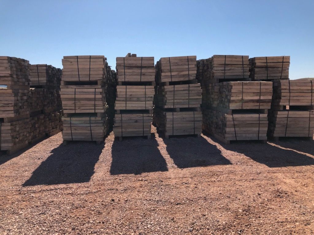 Stacks of weathered wooden pipeline skids in an industrial yard under a cloudy sky