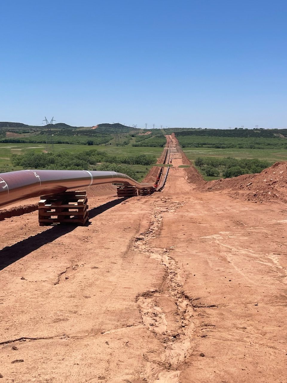 Pipeline stringing stretching into the distance beside a grassy field and blue sky