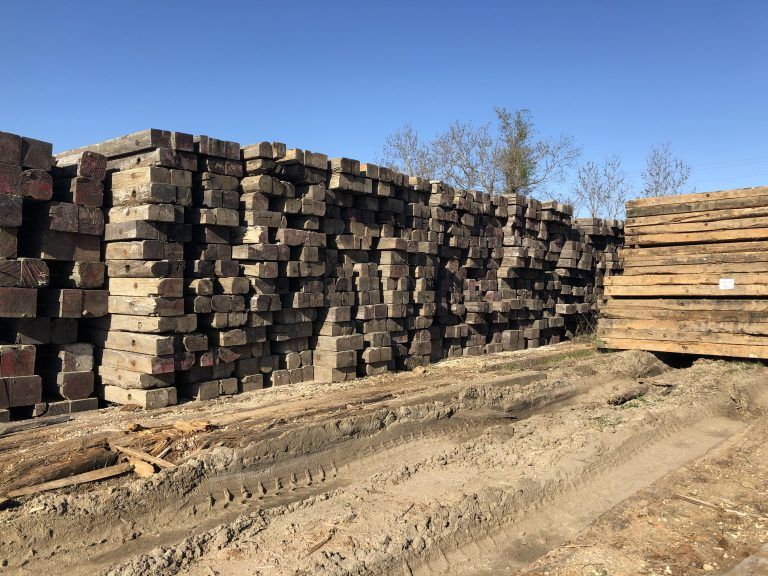 Stacks of wooden mats in an outdoor lumber yard under a clear blue sky
