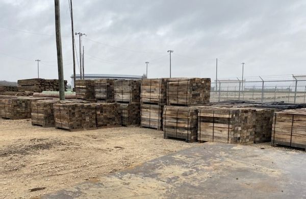 Stacks of weathered wooden pipeline skids in an industrial yard under a cloudy sky