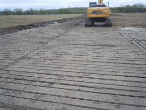 Yellow bulldozer on a laminated mat road in a muddy field under a cloudy sky