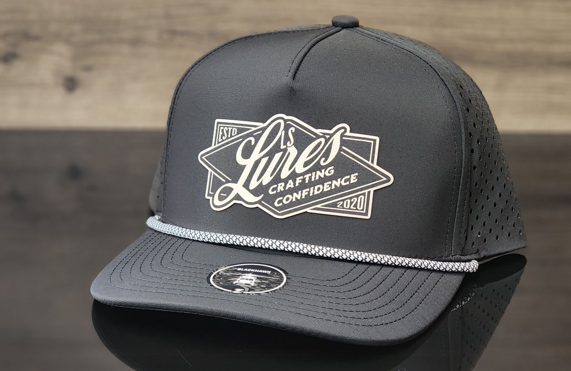 Dark gray mesh cap with white script logo on the front, shown on a wooden surface.