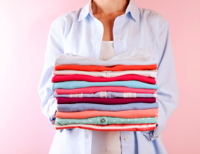 Woman with white shirt and blue button-down shirt holding a stack of multi-colored folded laundry.