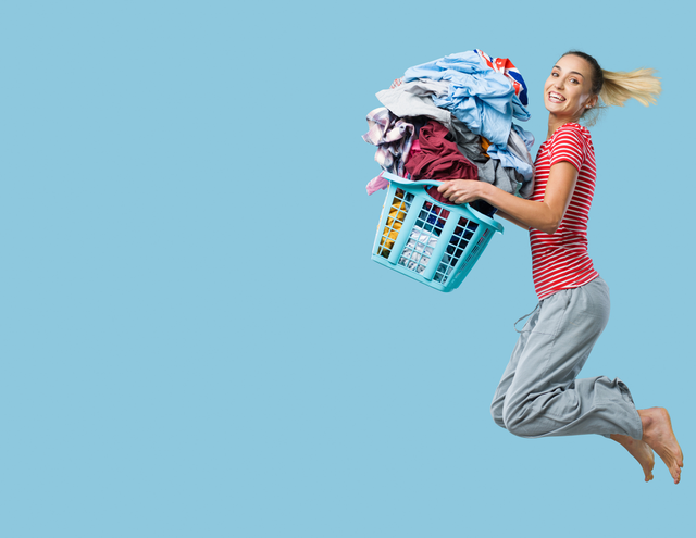 Woman in red striped shirt and green pants jumping in the air with wash and fold laundry in laundry basket.