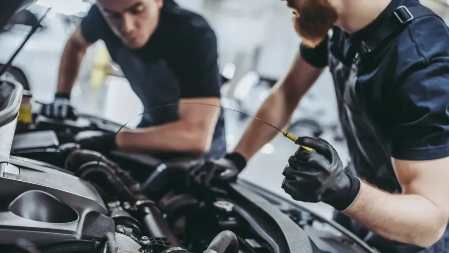 Two auto mechanics checking engine oil with a dipstick