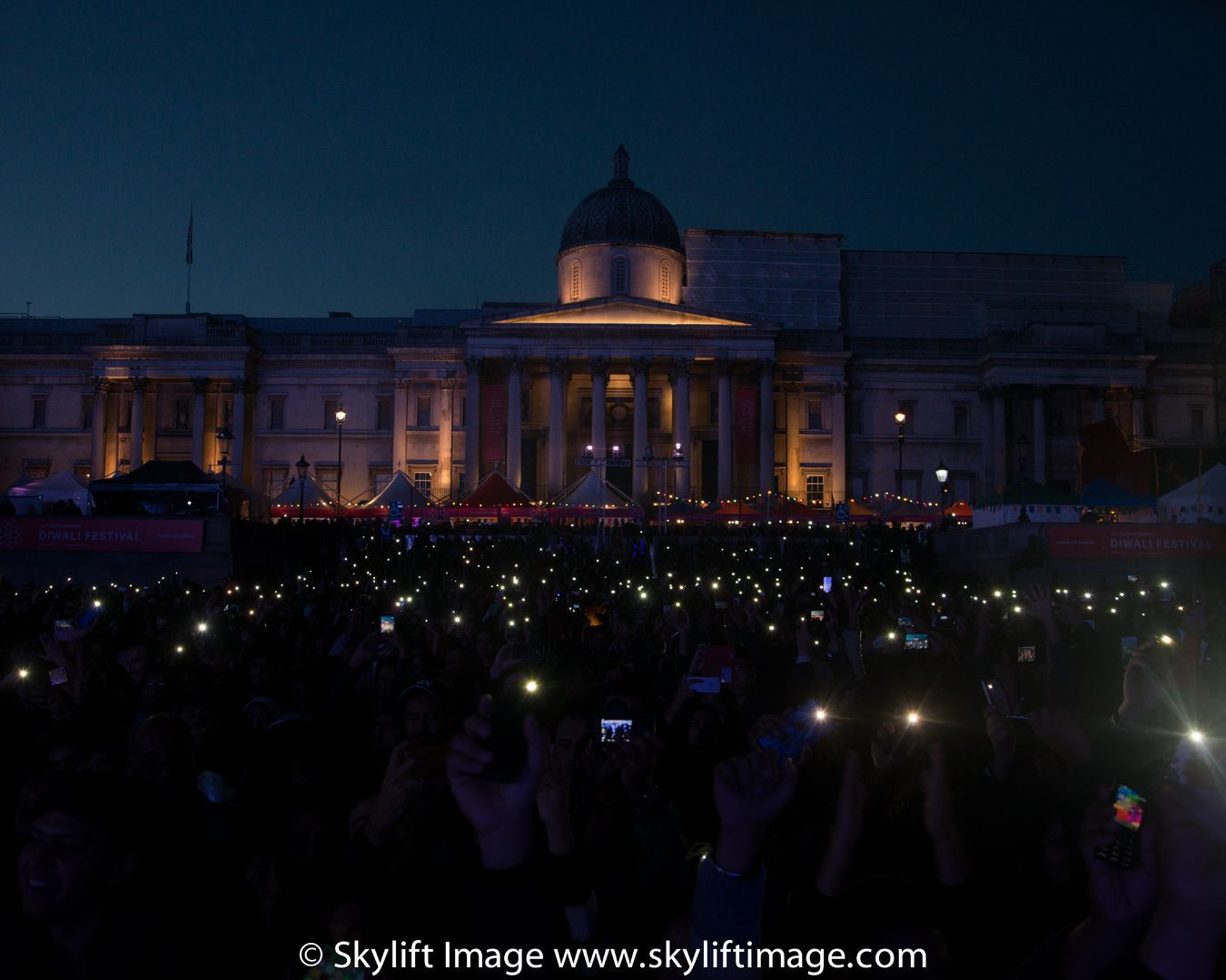Thousands of phone lights held up by the crowd on Trafalgar Square at dusk, in front of the National Gallery