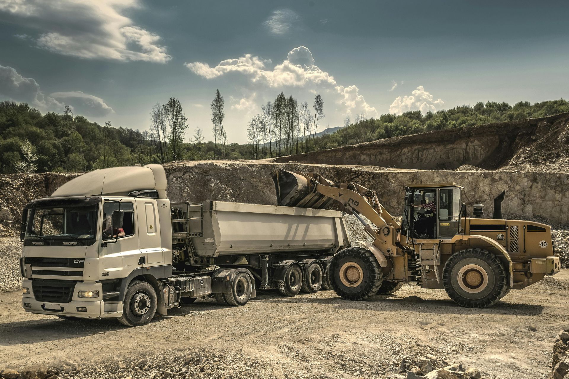 A front loader filling a dump truck with dirt at a quarry.