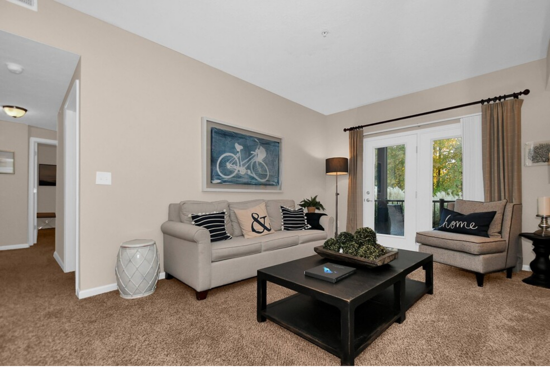 Bright living room with beige sofa, black coffee table, armchair, and large window with curtains