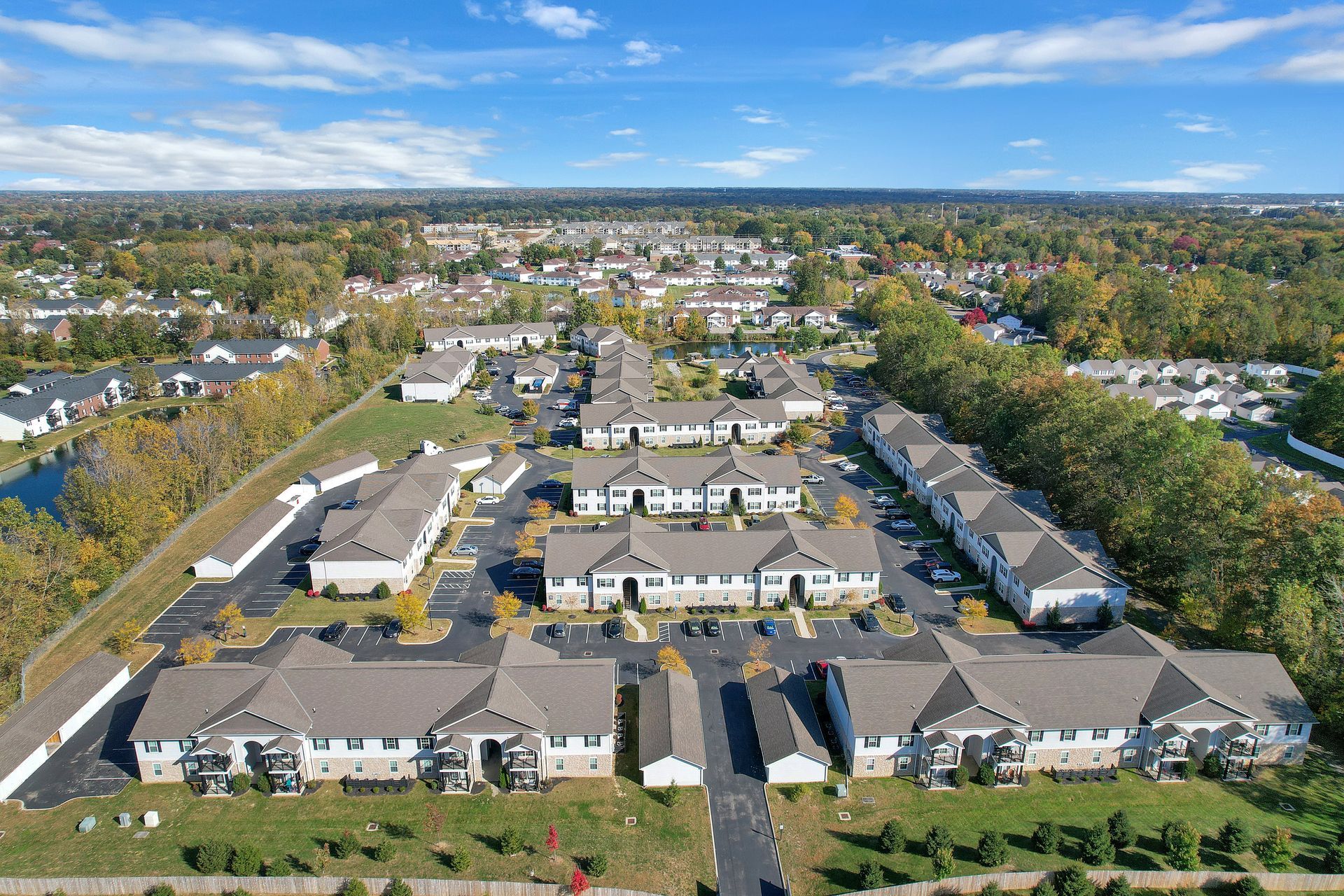 Aerial view of a large apartment complex with parking lots and trees in a suburban neighborhood.