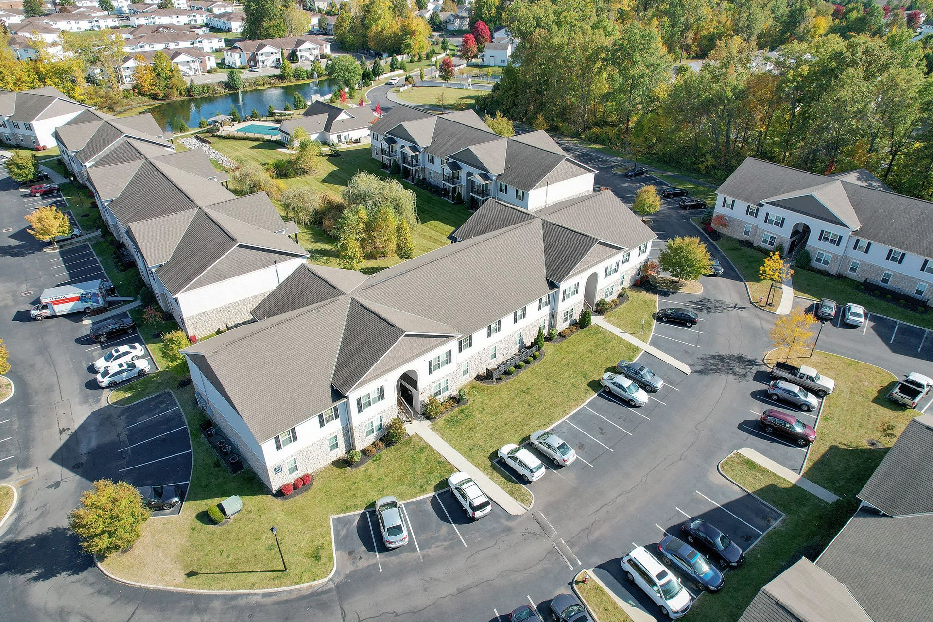 Aerial view of a large beige apartment complex with parking lots and surrounding trees.