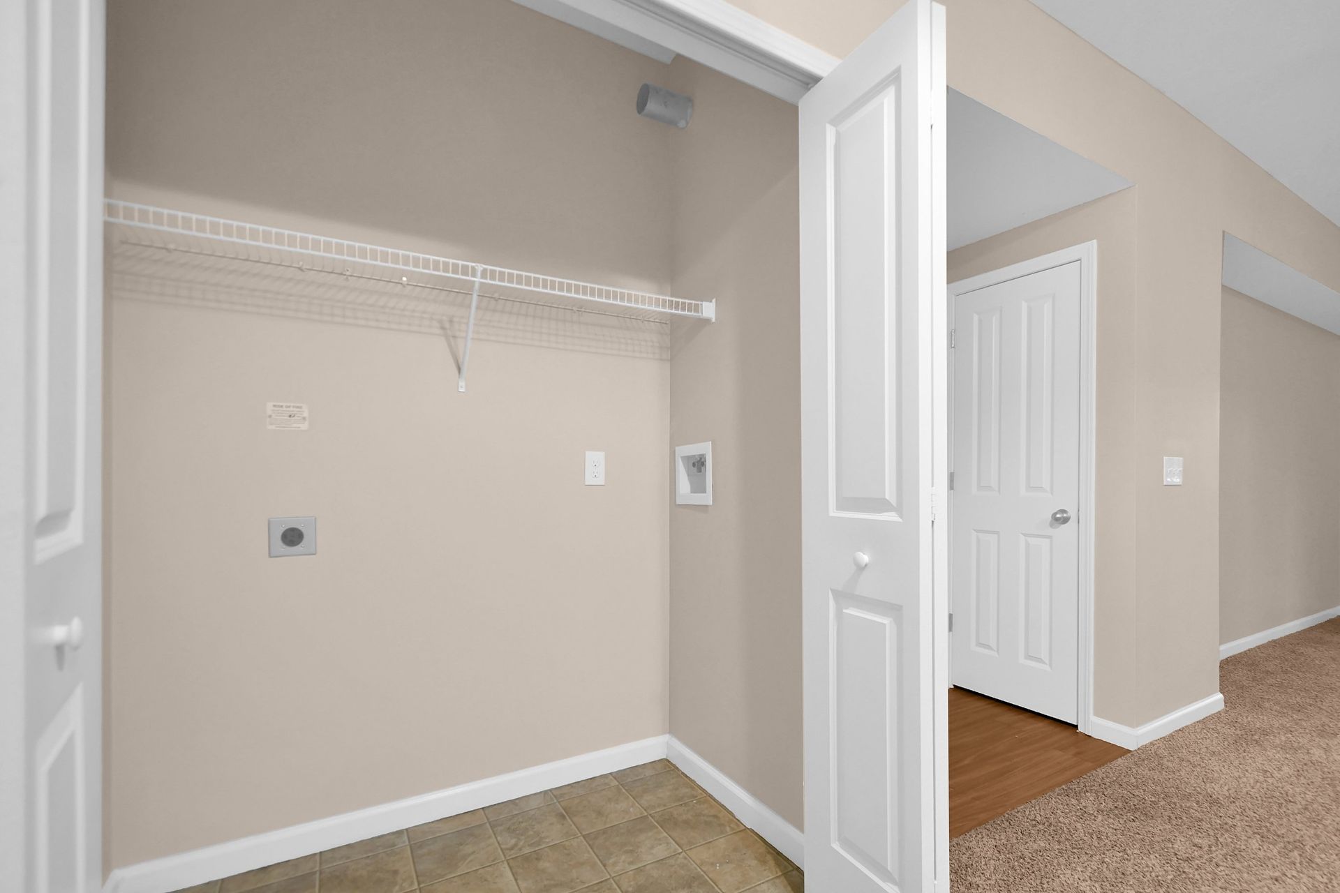 Empty beige walk-in closet with wire shelving and open double doors leading to a carpeted hallway.