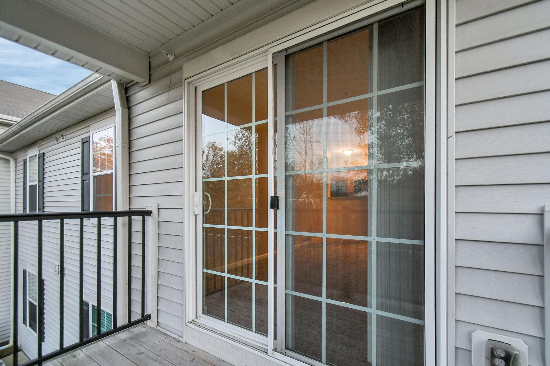Apartment balcony with sliding glass door, white siding, and black railing at sunset