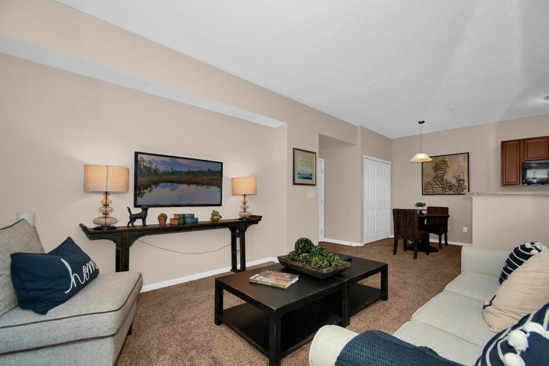 Bright living room with beige walls, dark coffee table, sofa, console table, and dining nook in the background