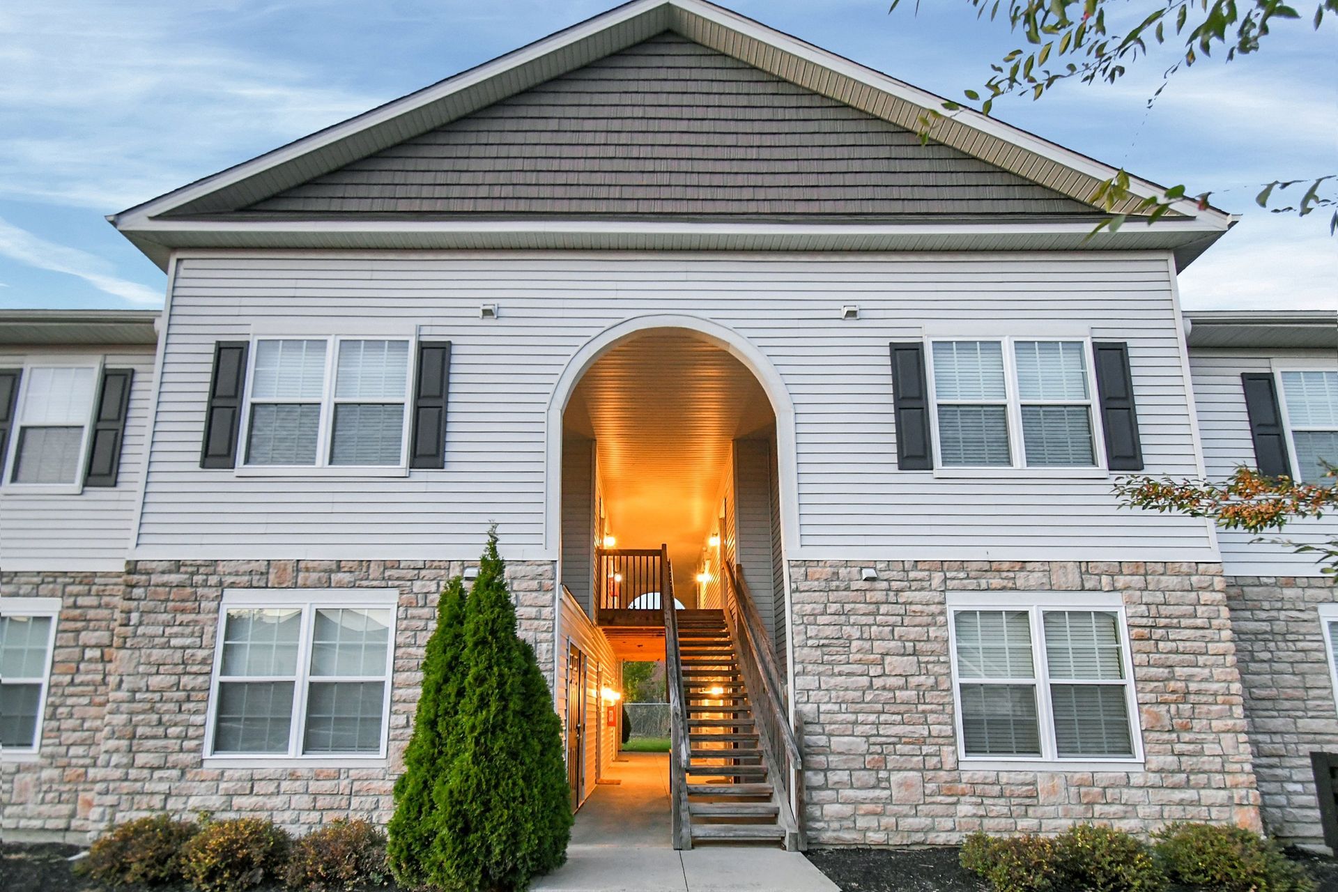 Front view of a white house with stone lower facade and illuminated arched entryway at dusk