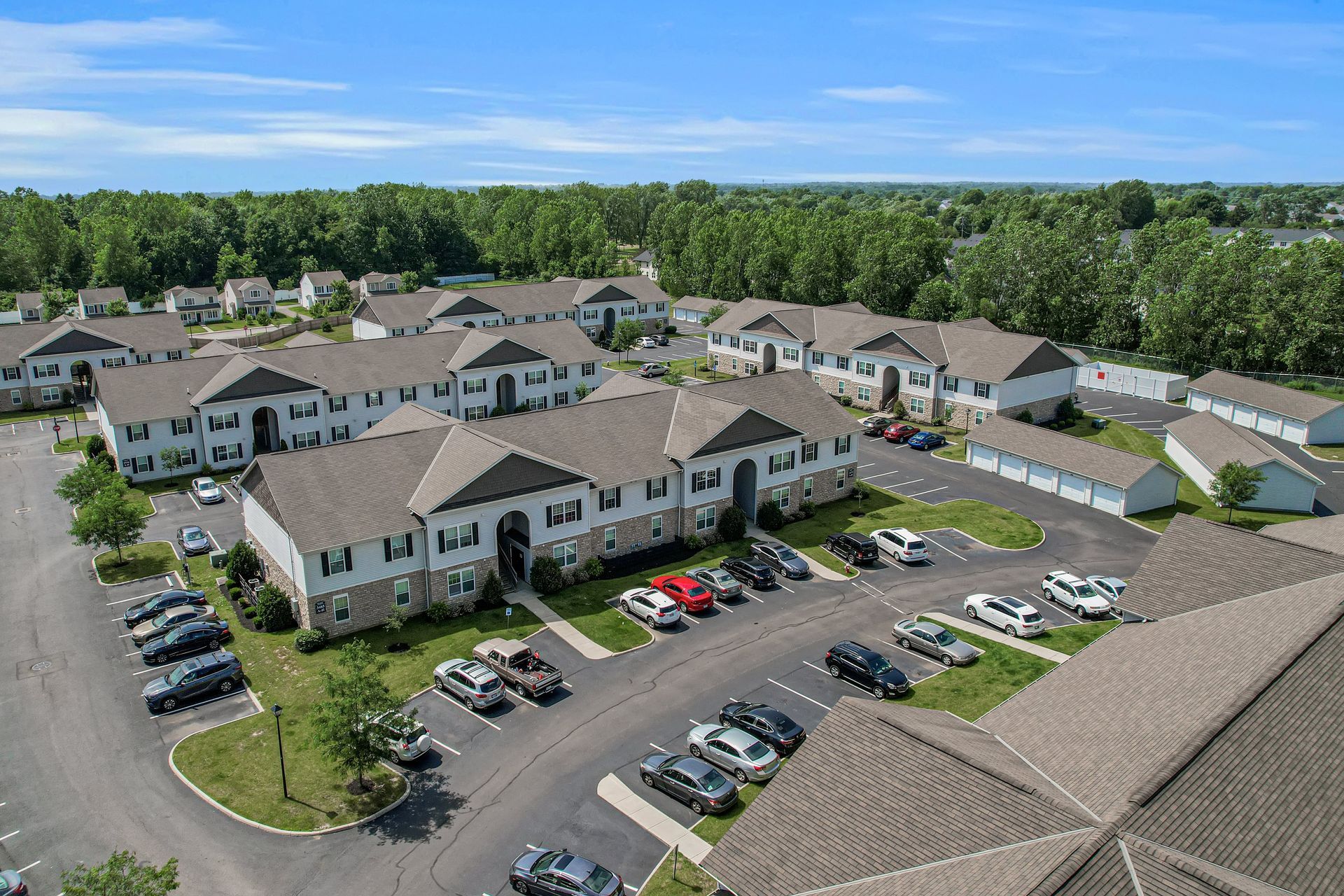 Aerial view of a large apartment complex with parked cars and surrounding trees on a sunny day