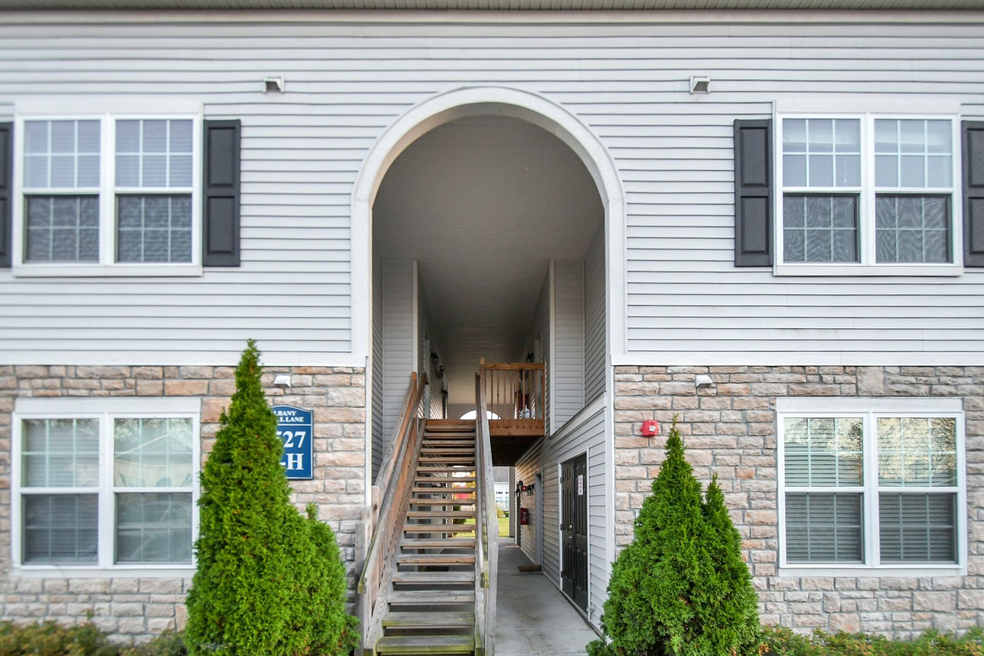 Apartment building entrance with central archway, stairs, and windows, framed by shrubs