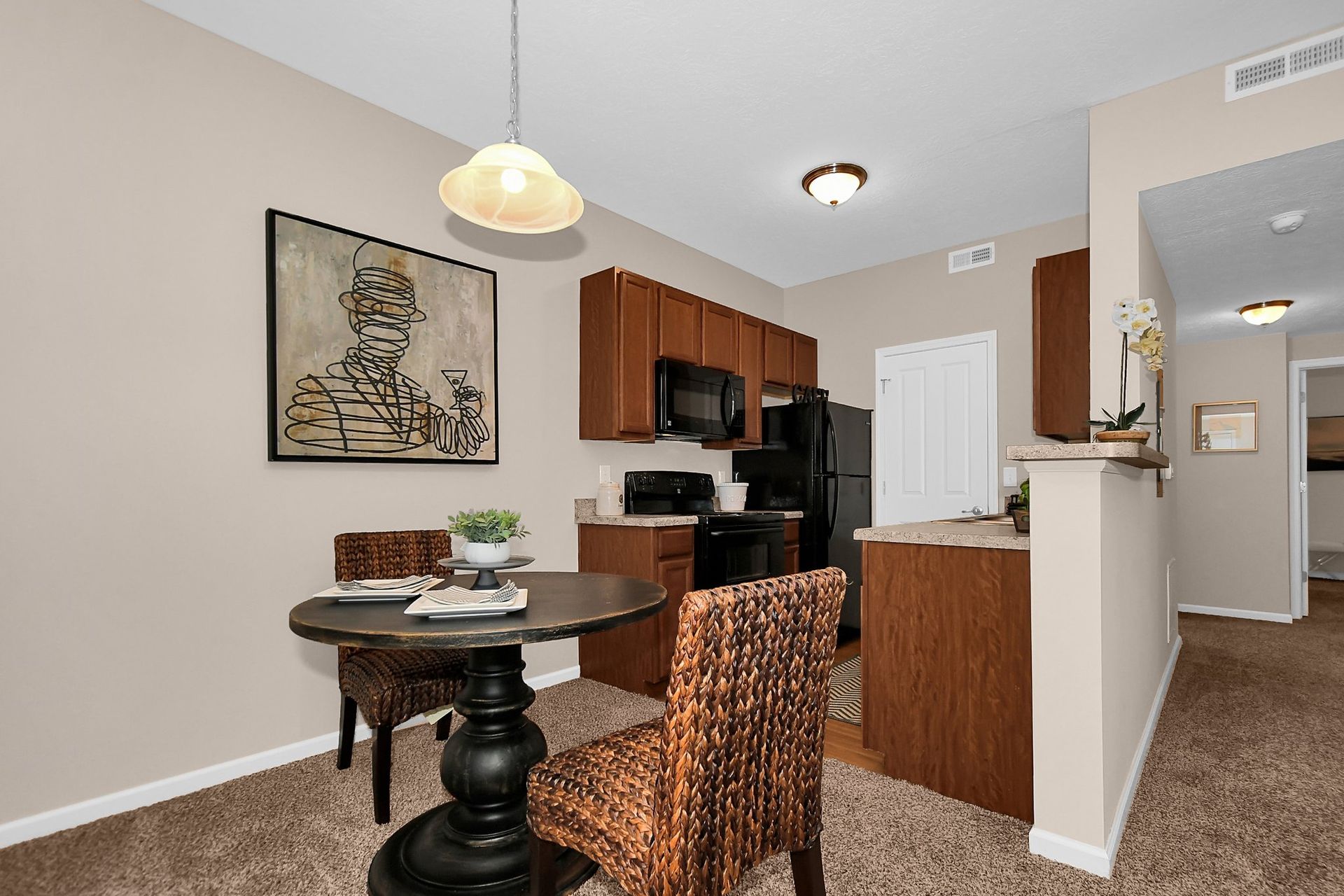 Open kitchen and dining area with wooden cabinets, round table, and patterned chair in a beige apartment.