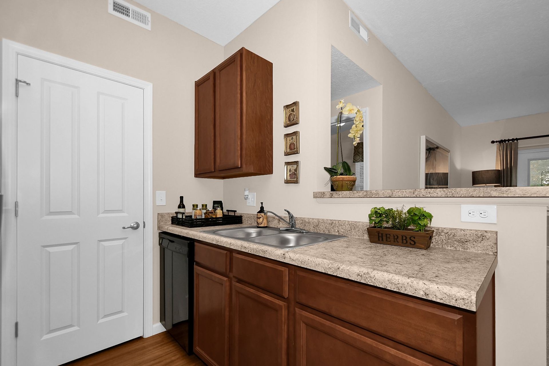 Kitchen counter with sink, brown cabinets, granite countertop, and a white door beside a pass-through opening