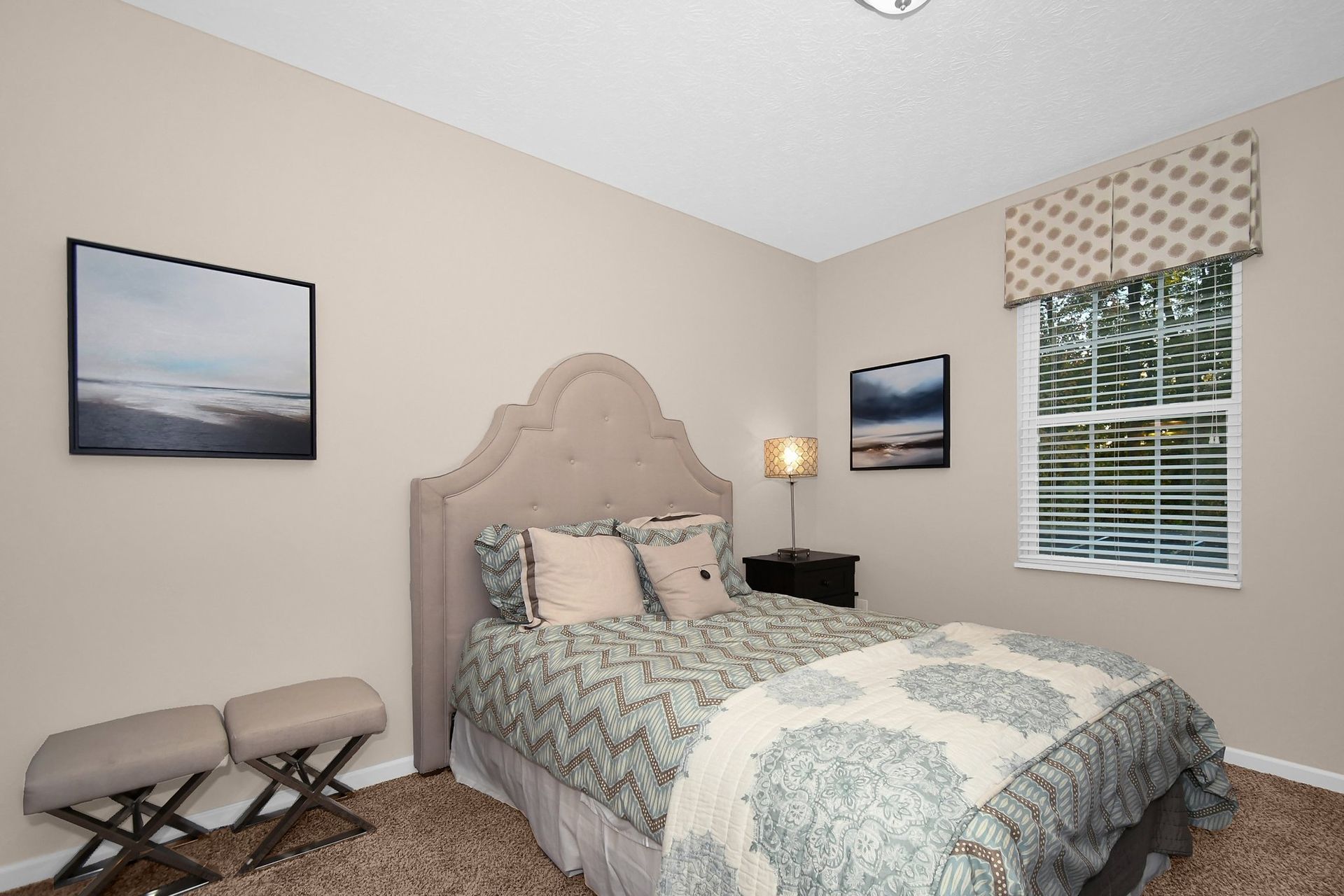 Cozy bedroom with a bed, nightstand lamp, window, wall art, and upholstered bench.