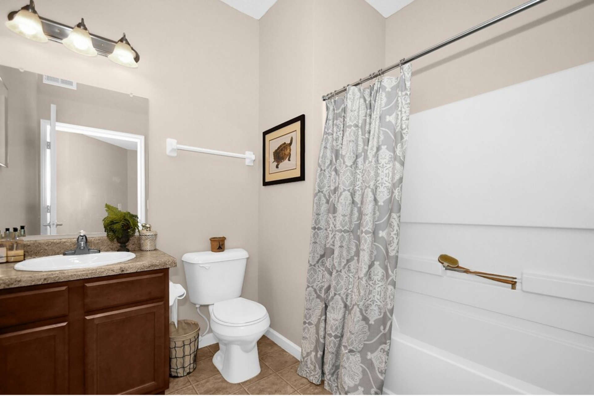 Bathroom with wood vanity, toilet, mirror light, and shower/tub with gray curtain