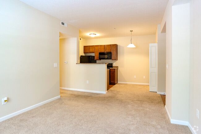 Empty beige apartment living room with carpet, open kitchen, and pendant light