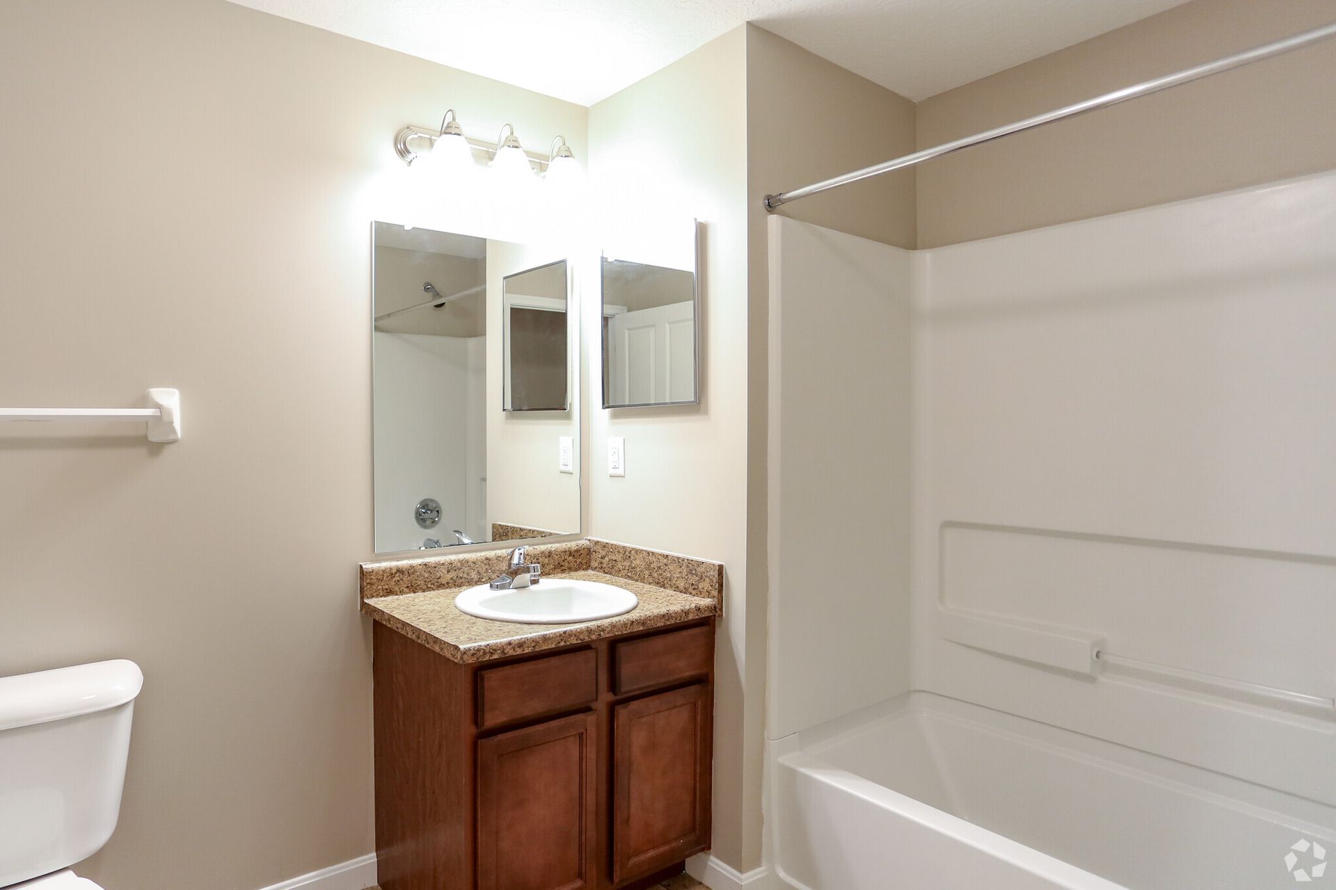 Small bathroom with vanity, mirror, sink, toilet, and white bathtub/shower combo.