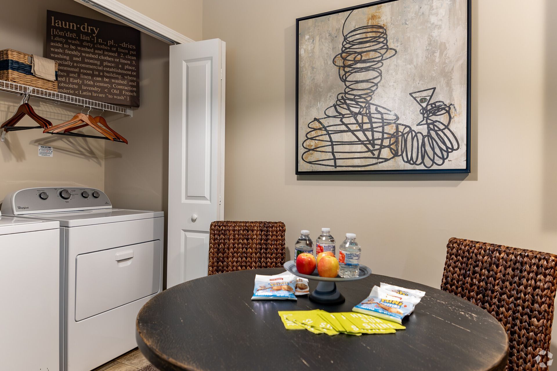 Small dining area with round table, woven chairs, laundry nook, and abstract wall art