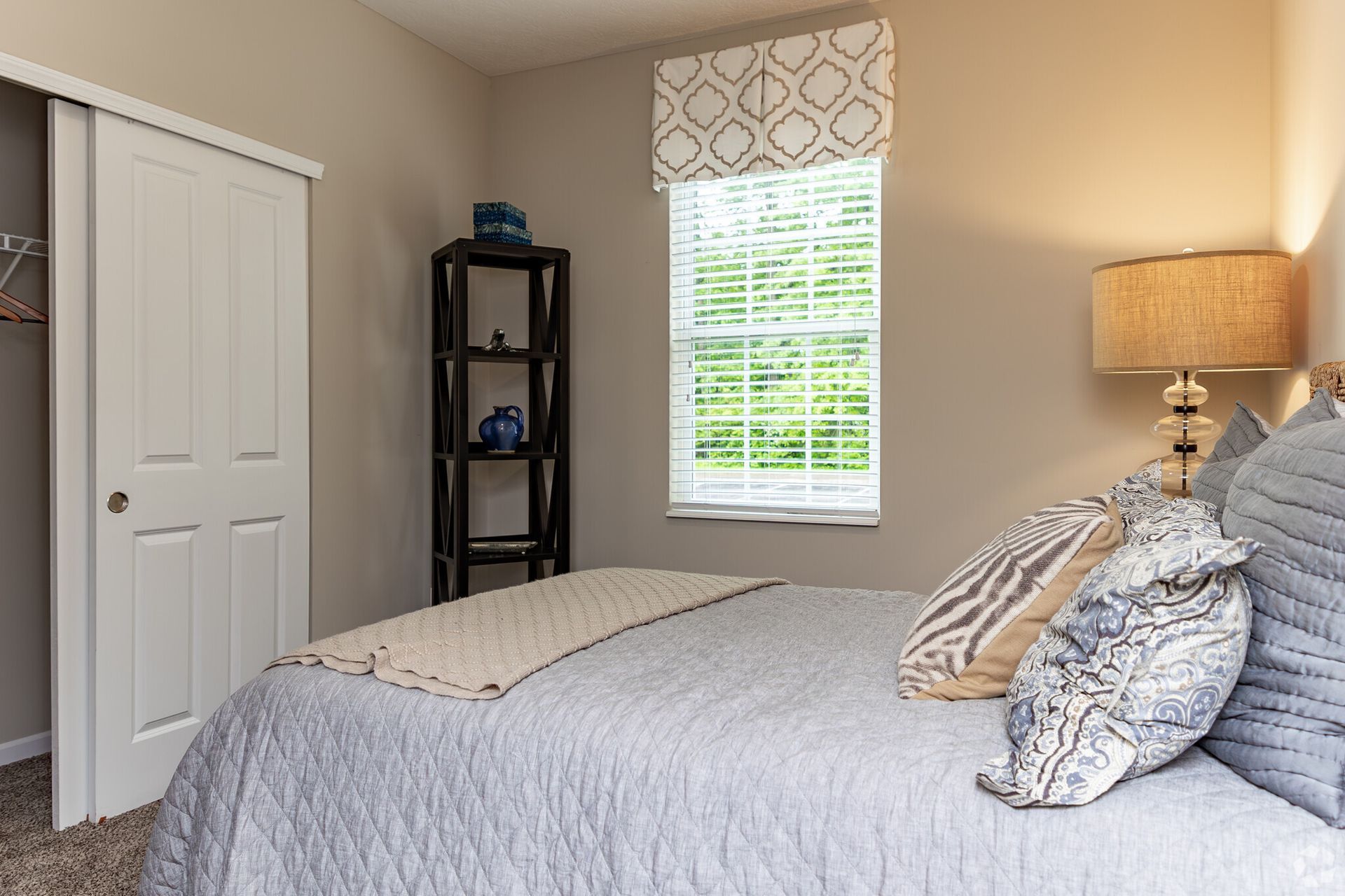 Bright bedroom with a bed, white closet, window, and lamp on a side table.