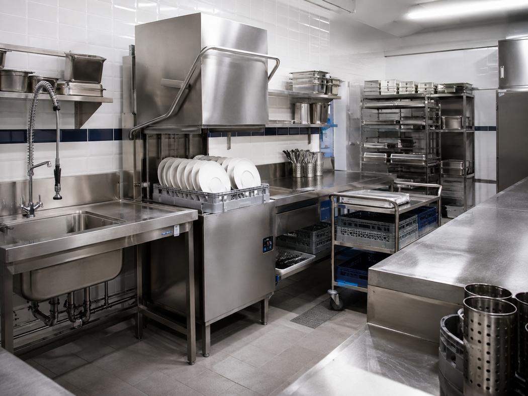 Cucina professionale in acciaio inox con lavelli, scolapiatti, piani di lavoro e scaffali in una zona di preparazione pulita.