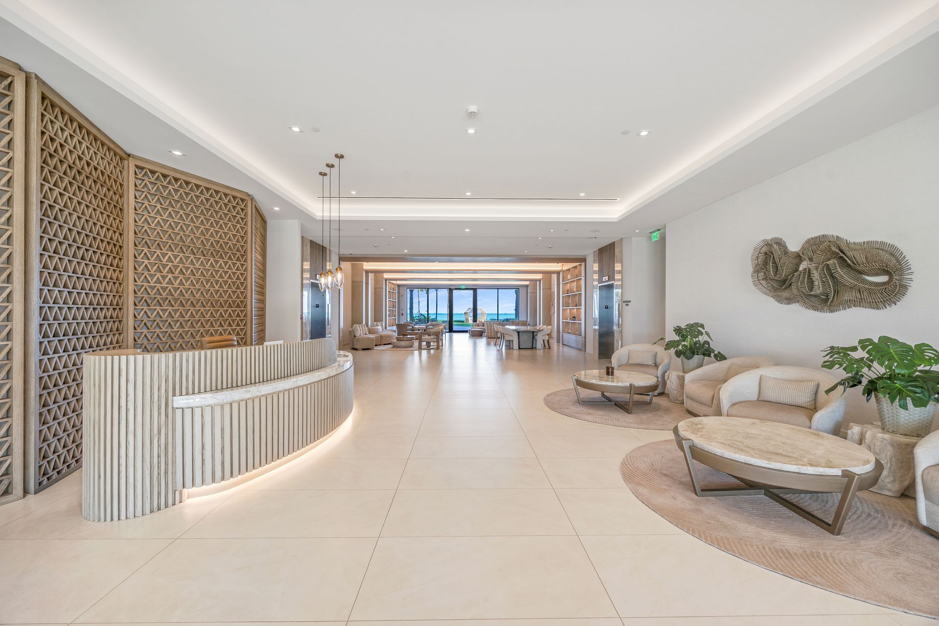 Bright modern lobby with curved reception desk, lounge seating, and tiled floor leading to ocean view in Aqualina Bahamas