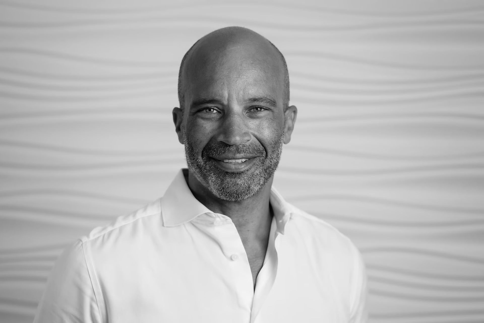 Jason Kinsale smiling in a white shirt, against a textured white background.