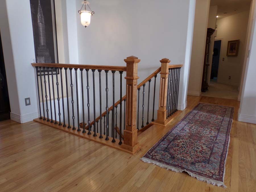 Light wood staircase with black iron spindles, rug, white walls, and a hanging light.