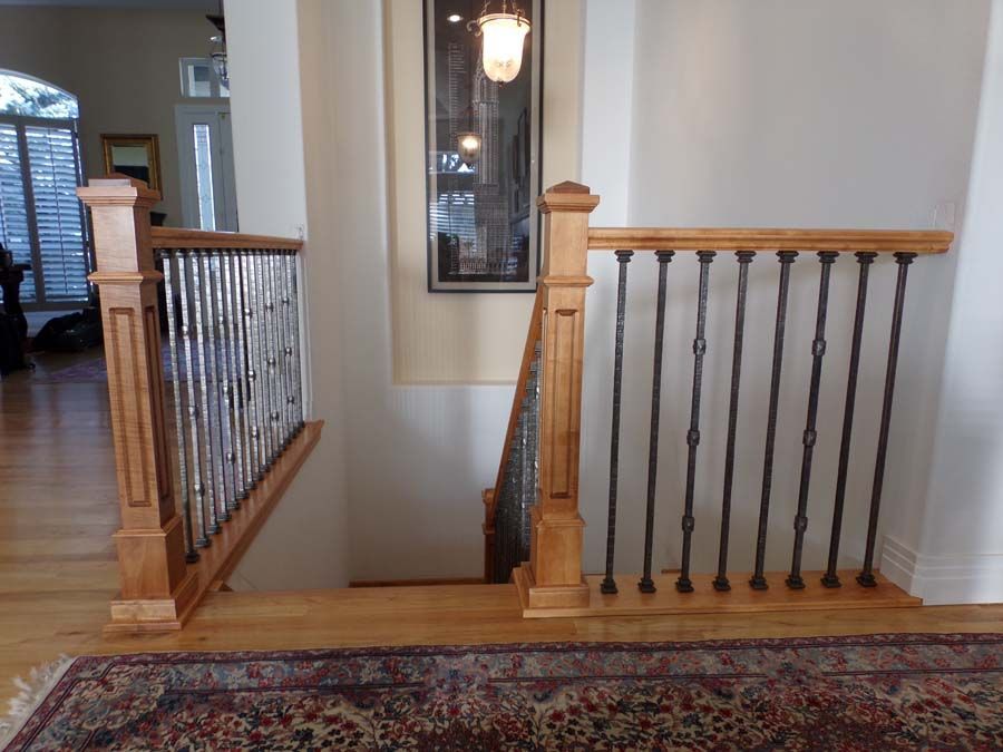 Wooden staircase with metal railings, light wood and white walls. A rug covers the floor.