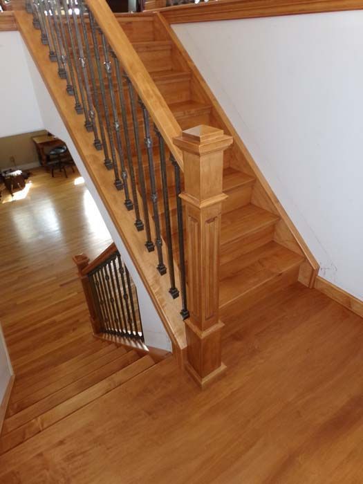 Wooden staircase with ornate black metal railing, leading up to a landing.
