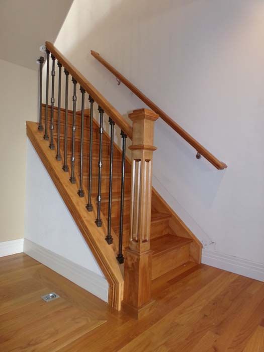 Wooden staircase with metal spindles, oak treads, and a banister, against a white wall.