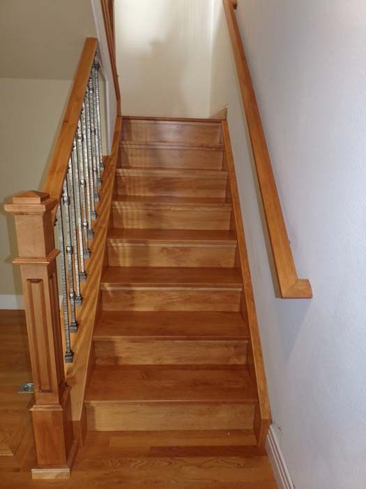 Wooden staircase with metal spindles and a wooden handrail on a light-colored wall.