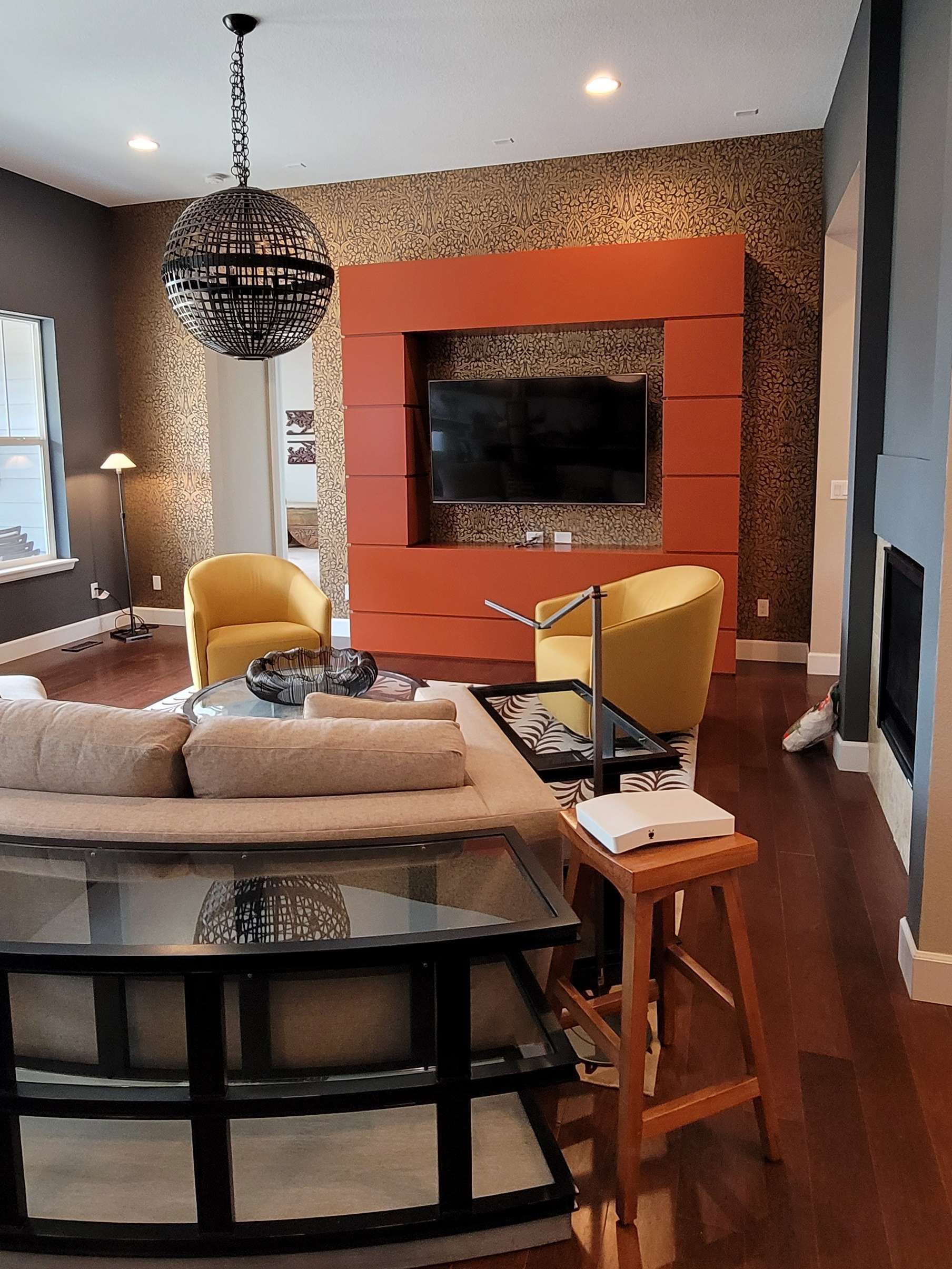 Living room with modern decor, orange wall-mounted TV, yellow chairs, dark sofa, and patterned accent wall.