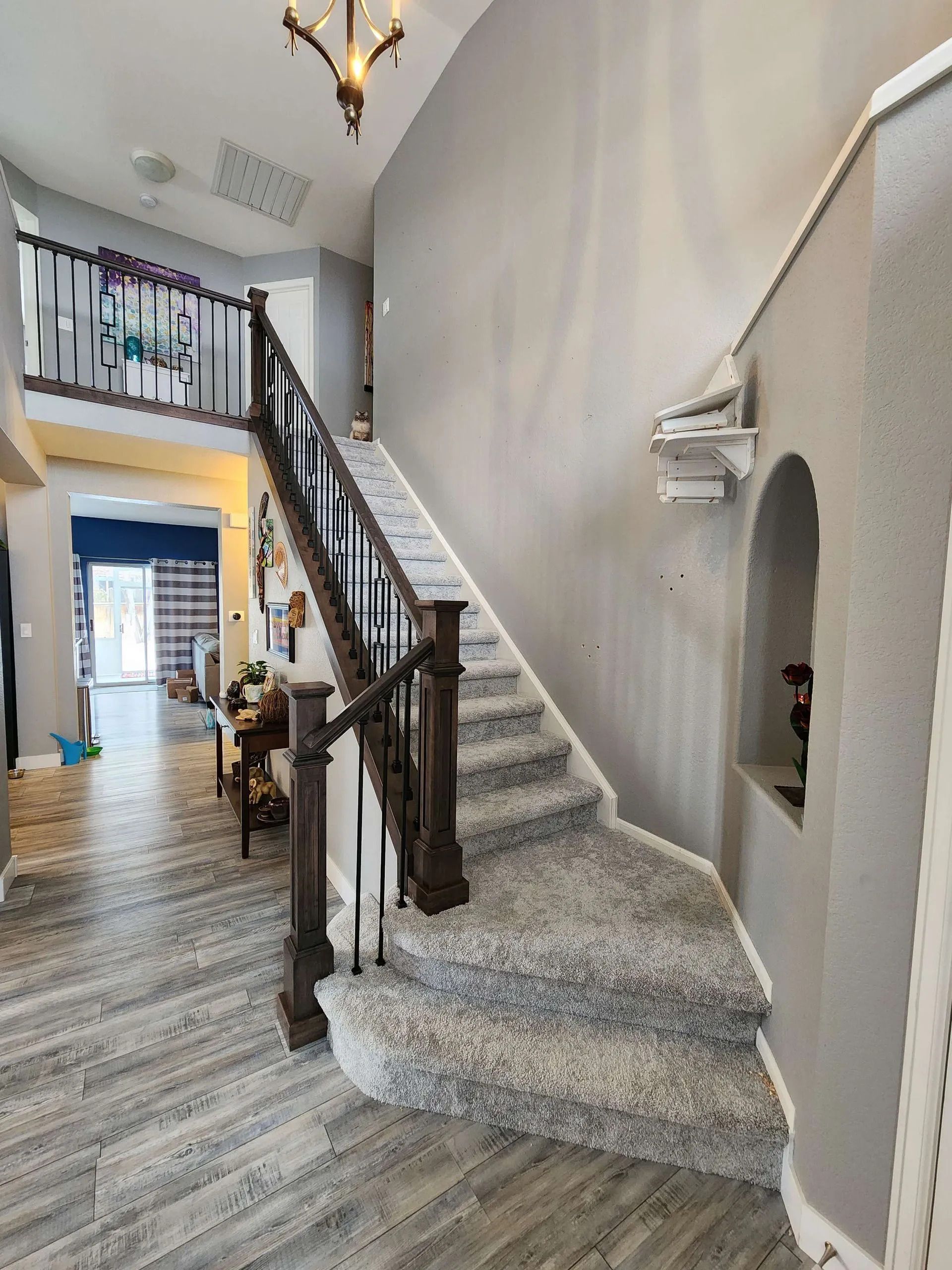 Staircase with carpeted steps and dark wood railing, leading to a second-floor balcony, with a tiled floor hallway.