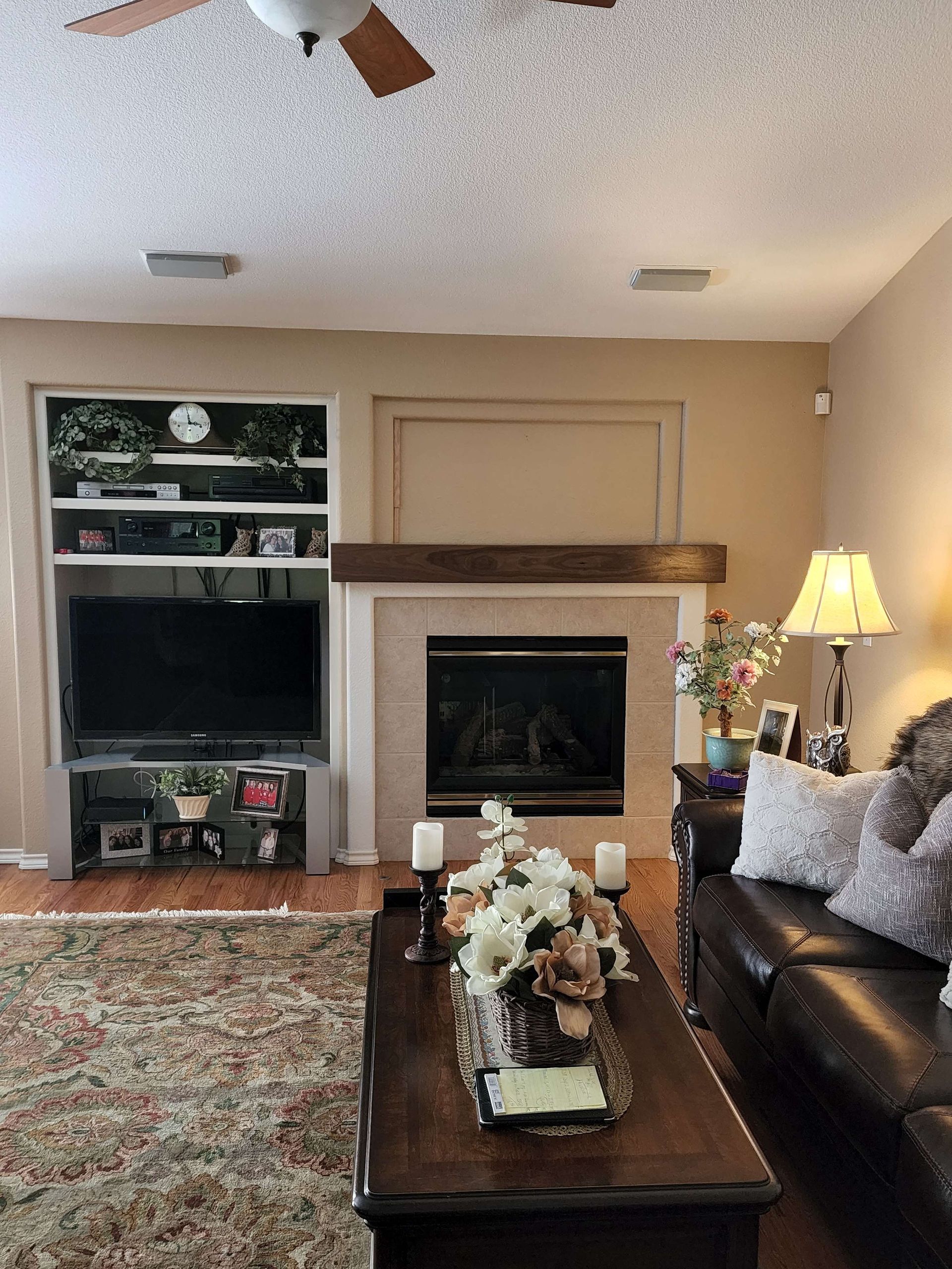 Living room with fireplace, built-in TV, brown leather sofa, and floral decorations.