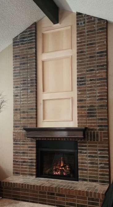 Brick fireplace with dark trim and wooden paneling in a living room. Fire burning inside.